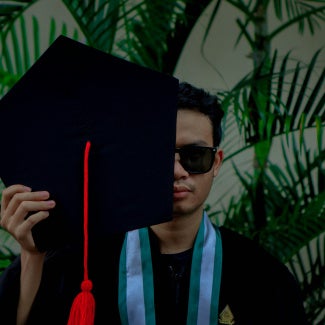 Man holding Master's graduate cap in front of his face