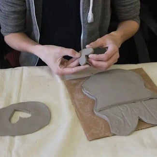 Hands forming clay pottery on a work table